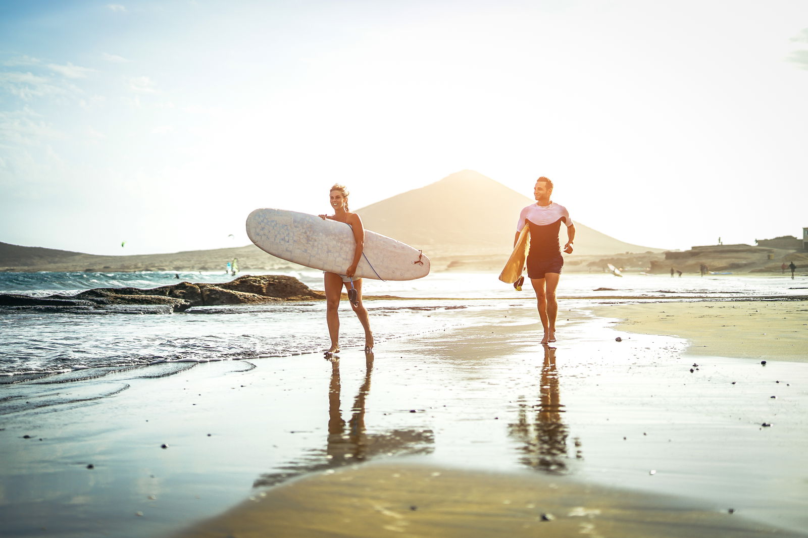 Männer und Frauen gehen am Strand mit einem Surfbrett