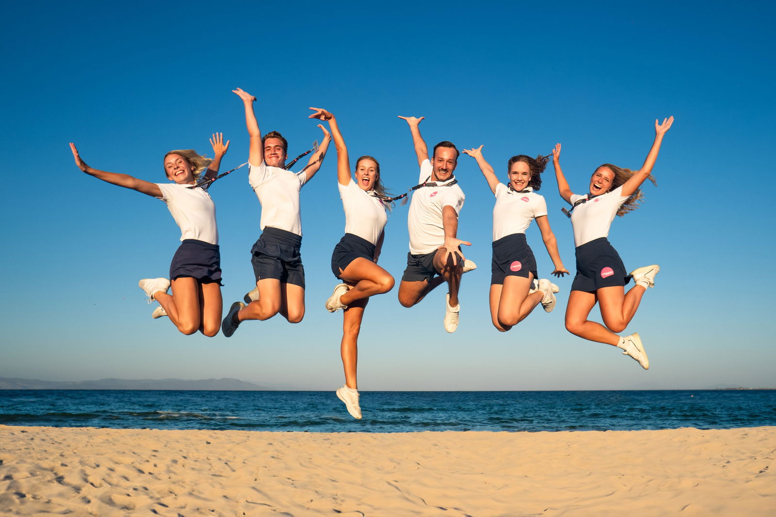 Team von Entertainern springt am Strand in die Luft