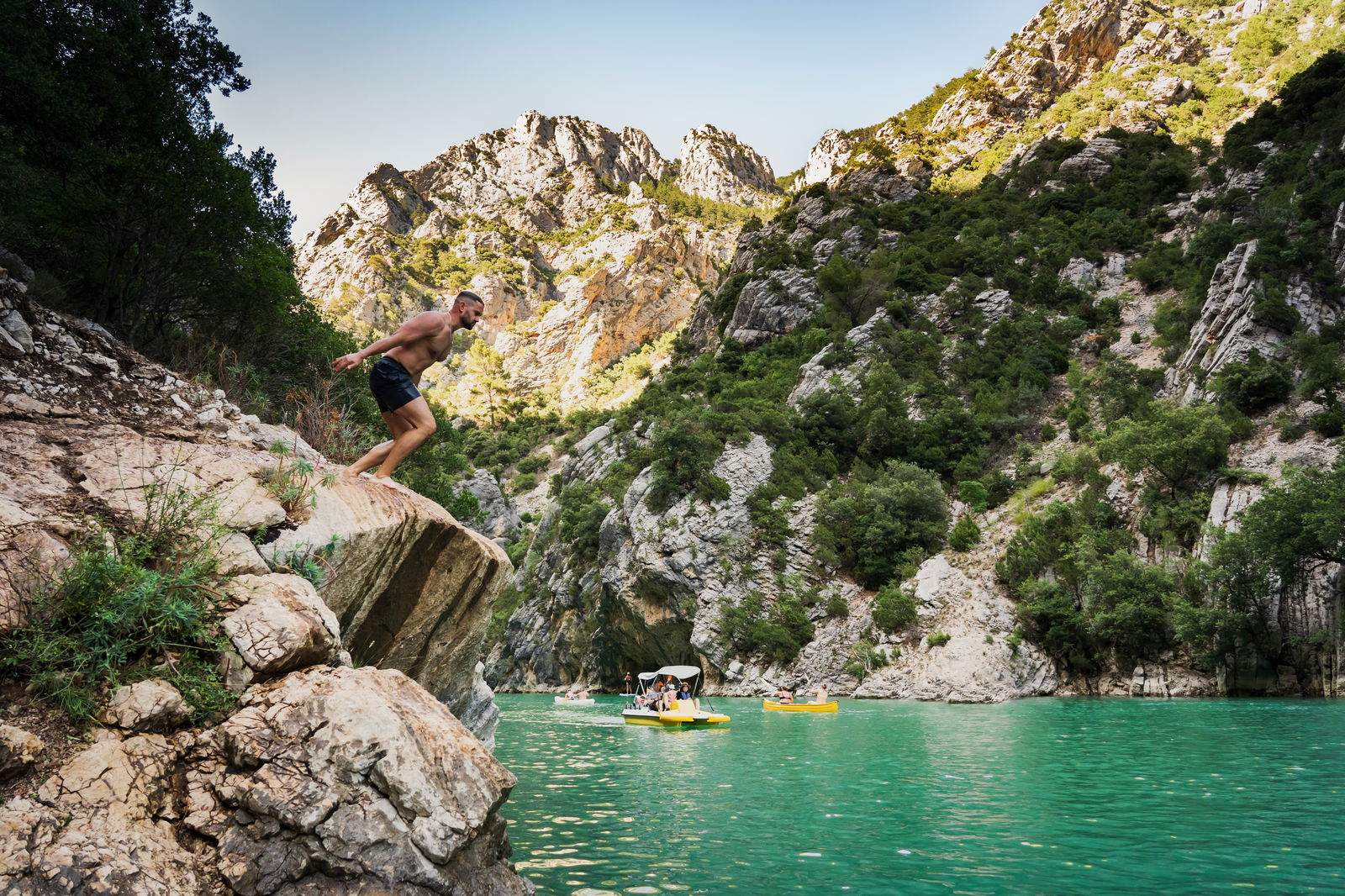 young man with athletic build prepares jump into water from cliff lake verdon